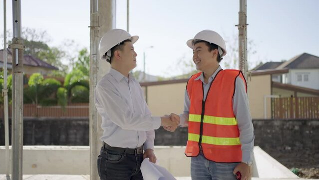A male engineer and a male construction supervisor shake hands with delight after inspecting the construction work.