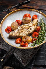 Grilled halibut fish steaks with tomato and potato in plate. Wooden background. Top view - obrazy, fototapety, plakaty