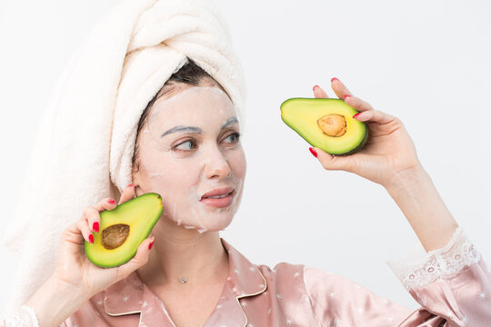Face care and beauty treatments. Woman with a sheet moisturizing avocado mask on her face isolated on white background.