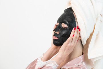 Face care and beauty treatments. Woman with a sheet moisturizing charcoal mask on her face isolated on white background