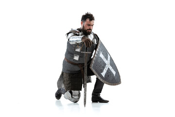 Portrait of serious manm medieval warrior, knight in special protective covering sitting on one knee isolated over white background - obrazy, fototapety, plakaty