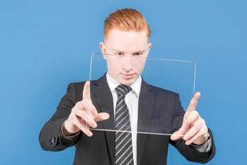An office worker. Seller. Businessman. Businessman. Boss. Portrait of a young red-haired man in a suit and with a tablet in his hands on a blue background
