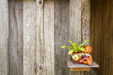 Selective focus of wooden wall with a small clay pot and a tree at the bottom right of the picture.