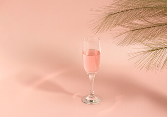 Creative idea,  glass of wine with shadow and green branches of leaves. Minimal concept of drinks on pink background.