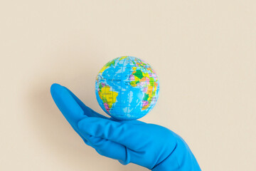 Earth globe in hands in blue protective glove on a clean beige background. The concept of protecting nature, ecology and global peace. World globe in Hand. The COVID-19 pandemic