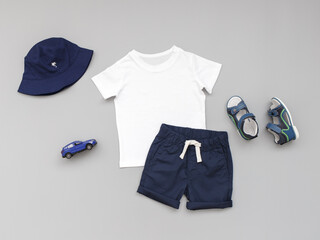 White t-shirt, blue shorts, sandals and panama hat on grey background. Children's clothing. Summer outfit for a boy. Flat lay, top view.