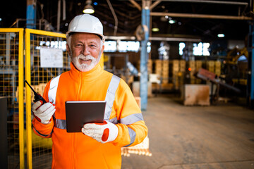 Portrait of blue collar worker with tablet computer standing in factory by the production machine.
