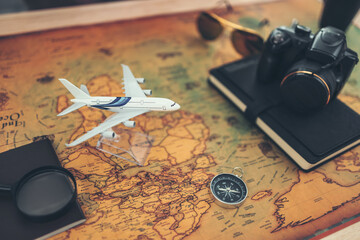 Hands playing model airplane to fly above world map and book, magnifying glass, compass and camera on map. Travel , Adventure and Discovery concept.