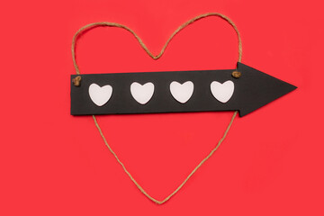 Black wooden arrow with white hearts and heart shaped rope on red background. Love valentine concept. Flat lay