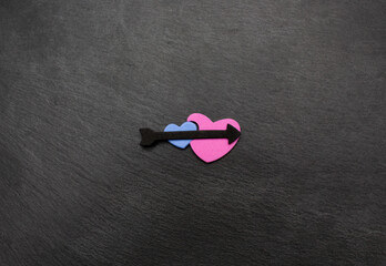 Blue and pink hearts with black arrow on black stone plate. Love valentine concept. Flat lay