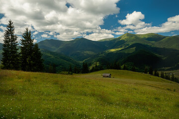 Green mountain landscape and an old wooden shed in a clearing.