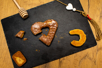 A piece of cookies, spoon for honey, heart shape cookie and white hearts on black stone plate. Love valentine concept. Flat lay