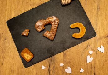 A piece of cookies, spoon for honey, heart shape cookie and white hearts on black stone plate. Love valentine concept. Flat lay
