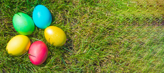 Fototapeta na wymiar A festive banner with a place for text, a top view of a bunch of colorful Easter eggs laid out on the green spring grass. Flat style, Easter holiday concept