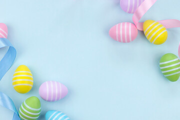 Top view of Easter eggs in pastel colors with blue and pink ribbons on light blue background. Flat lay image