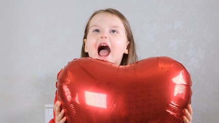 little cute girl in a red dress hides behind a red heart shaped balloon. valentines day concept