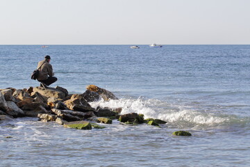 fishing a fisherman sits on the rocks with a spinning rod on the seashore