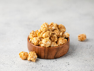 Caramel tasty popcorn in a wooden mango bowl on a light background. Sugar fast food snack on a table.