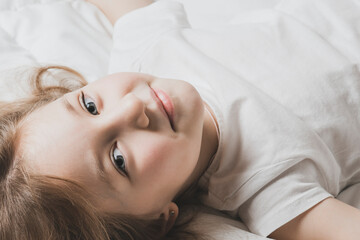 Fototapeta premium Beautiful little girl is lying on bed with white linens. The warmth of home comfort.