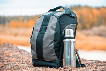 Hiking backpack with thermos for tea on the river bank.
