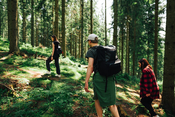 Group of young hipsters walk through a mountain forest, going up. Friends in stylish casual clothes on a hike go through the mountain forest