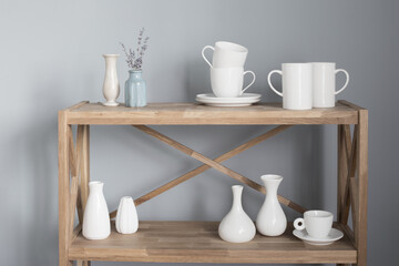 Fototapeta na wymiar white cups and vases on wooden shelf on gray background