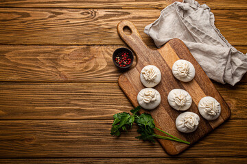 Raw freshly made Khinkali, traditional dish of Georgian Caucasian cuisine, dumplings filled with ground meat on white plate with herbs on wooden rustic background table top view space for text
