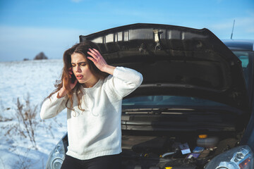 Broken down car troubles. Broken car outside on winter road. Confused young beautiful woman trying...