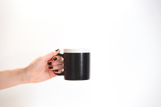 Black Coffee Mug Mockup For Design Demonstration. Stylish Cup Mock Up In Female Hands On White Wall Background.