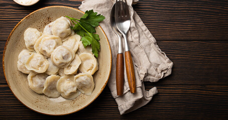 Fototapeta na wymiar Pelmeni, traditional dish of Russian cuisine, boiled dumplings with minced meat filling on plate with sour cream sauce on wooden rustic background table from above food composition