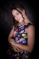 An attractive slim female model with long brown auburn hair wearing a flowery dress on a black background looking happy and smiling at the camera