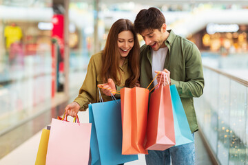 Excited Couple Shopping Holding And Looking At Bags In Hypermarket