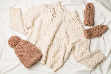 Sweater and winter hat withmittens on white bed sheet. Top view
