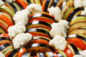 Ratatouille of freshly cut vegetables in a frying pan on a dark background