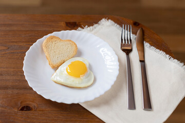 scrambled eggs in the shape of a heart on a white plate next to the appliances on a linen napkin.