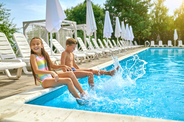 Children sitting near pool splashing water