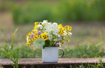 Beautiful wild flowers in white cup on wooden table and nature background.