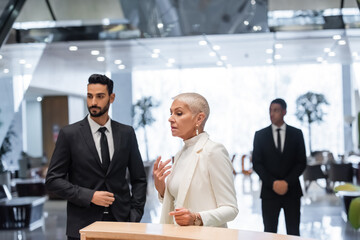 interracial bodyguards protecting mature businesswoman standing at hotel reception.