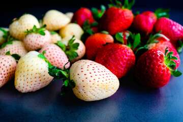 Close-up View of Whole Pineberries and Strawberries: Fresh red and white strawberries on a dark background