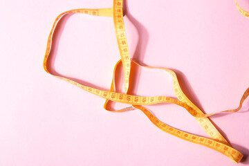 Bright yellow measuring tape isolated on a pink background