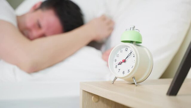 Asian attractive young man turn off alarm clock ringing in the morning