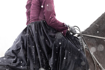 A female rider riding a horse in a long winter skirt and camisole. Close-up of the stallion's hand...