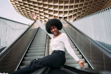 Smiling and playful young black woman sliding up an escalator railing