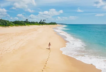 Foto op Aluminium Young female dressed in light summer clothes walking barefoot leaving footprints on the sand on Indian ocean Tangalle lonely coconut trees beach on Sri Lanka island. Aerial top view drone shot. © Soloviova Liudmyla