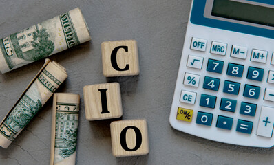 CIO - acronym on wooden cubes on a gray background with a calculator and banknotes.