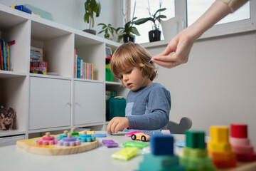 Beautiful toddler play with a plasticine and a wooden toys at home. Toddler play with a color educational toy. Child play at the table in the baby room with mother. Funny baby. Mother's hand.