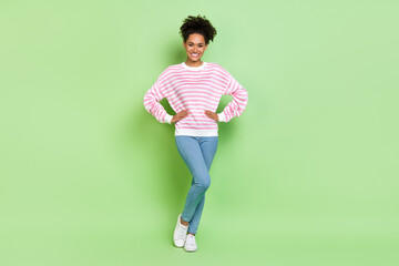 Photo of positive charming lady hands hips shiny smile wear striped shirt jeans isolated green color background