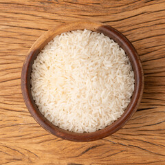 Raw white rice in a bowl over wooden table