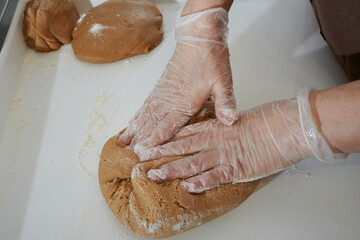 Confectioner in the process of preparing dough, hands in protective gloves in the process of working close-up. Rolling dough into a layer. Gingerbread Cooking Technology