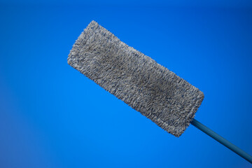 Generic plastic sweeping mop with a dirty textile sponge. Close up studio shot, isolated on blue...